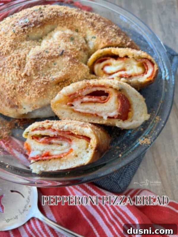 A large, golden-brown pepperoni pizza bread, coiled and sliced, viewed from above, with marinara sauce for dipping.