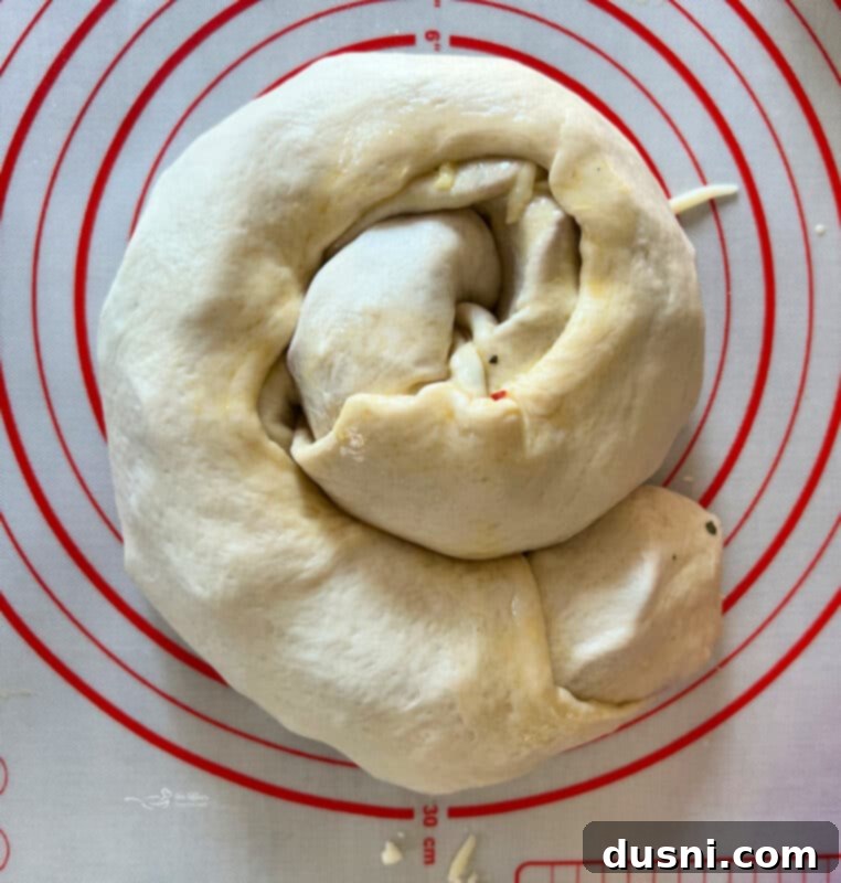 Pizza dough tightly rolled up with pepperoni and cheese inside, ready for coiling.