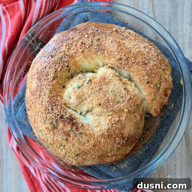 Coiled pepperoni pizza bread in a pie plate, brushed with egg wash and topped with Parmesan cheese and garlic powder, ready for baking.