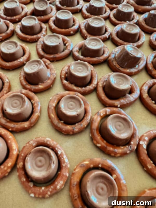 Rolo candies placed neatly into the center of each circular pretzel on a baking sheet.