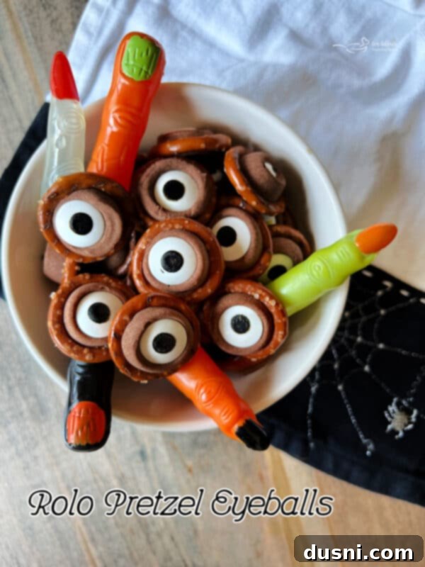 Close-up of Rolo Pretzel Eyeballs in a white serving bowl with plastic witch fingers as decoration.
