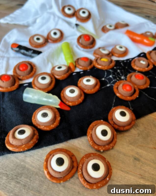 An overhead shot of Rolo Pretzel Eyeballs arranged on a white serving platter, some with plastic spider rings.