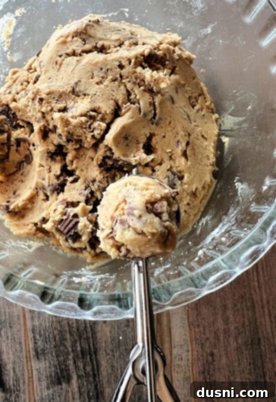 Ultimate Reese's Peanut Butter Cookies 6 A close-up of cookie dough being scooped onto a parchment-lined baking sheet using a small cookie scoop.