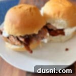 Texas Heat Smoked Brisket 19 Two spicy beef brisket sliders on a white plate, garnished with fresh herbs.