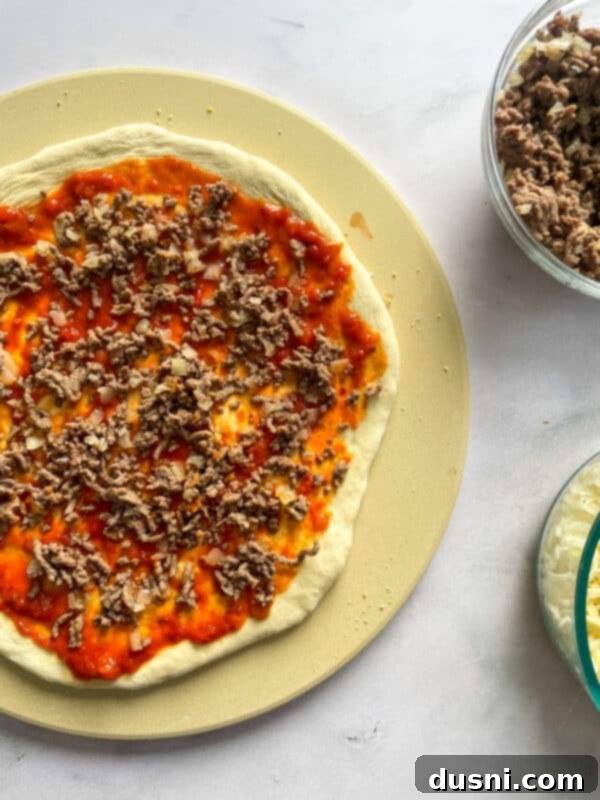 Pizza dough spread with sauce and ground beef toppings.