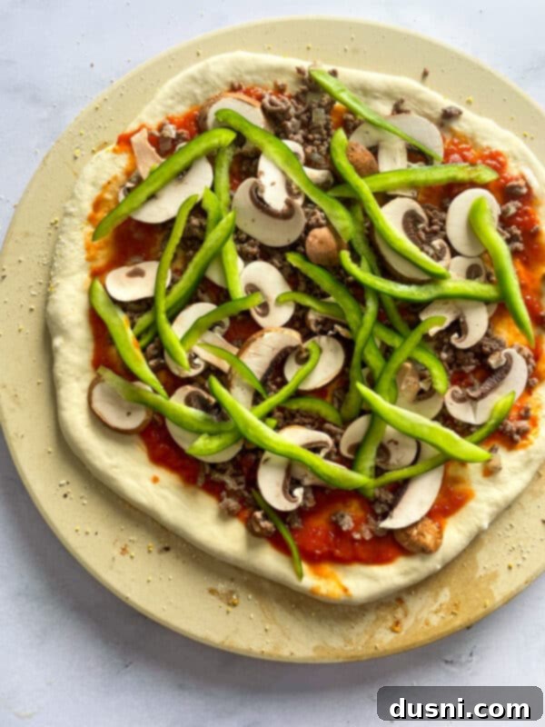 Adding mushrooms, peppers, olives, and pepperoni to a pizza base.
