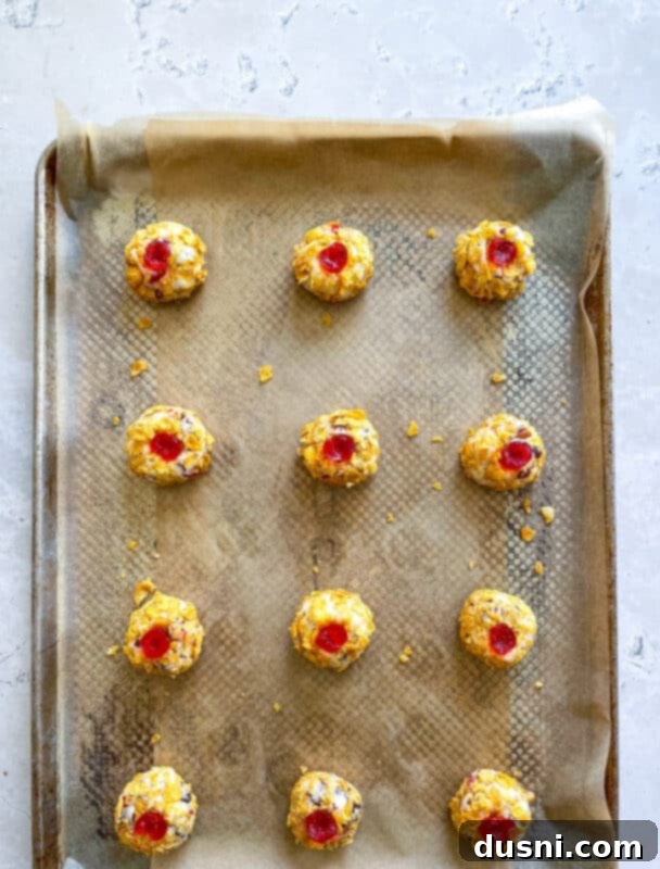 Maraschino cherry halves being pressed onto the cornflake-coated cookie dough balls.