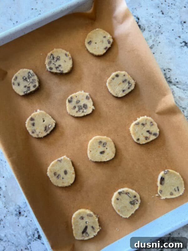 An Orange Ginger Refrigerator Cookie log being rolled in decorator sugar crystals on plastic wrap.