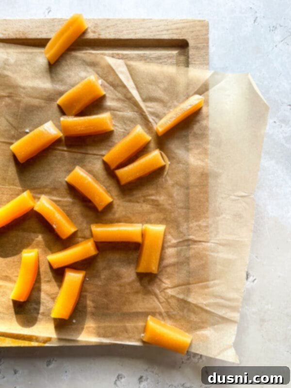 A batch of unwrapped homemade caramels on a wooden cutting board, with some cut in half.
