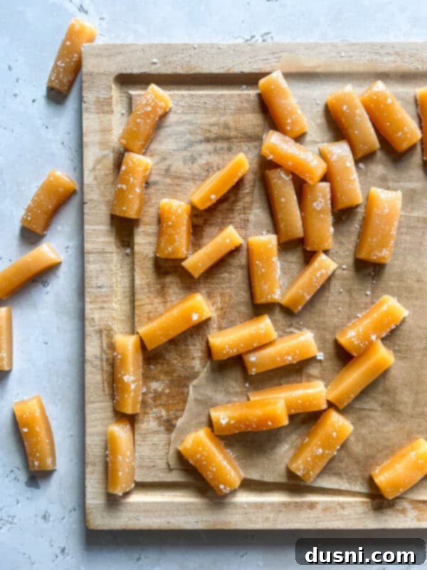 A close-up of golden caramel mixture being stirred in a heavy-bottomed saucepan with a wooden spoon.