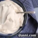 A serving of homemade Devonshire Cream in a blue bowl with a silver spoon, ready to be enjoyed with scones or desserts.