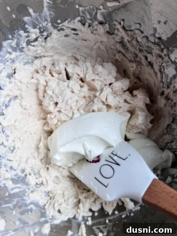 Sour cream being gently folded into the whipped cream mixture, creating a smooth, cohesive Devonshire Cream.
