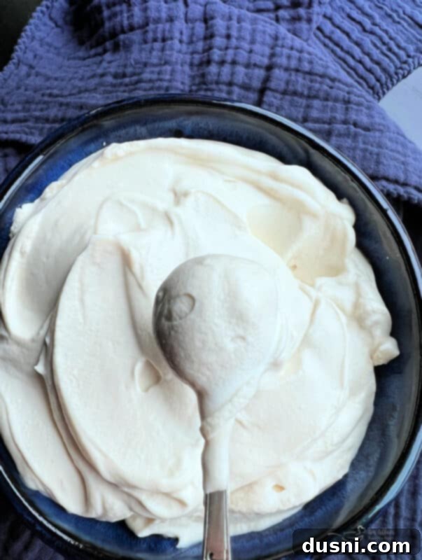 Homemade Devonshire Cream in a decorative blue bowl, showing its creamy texture, with a serving spoon and a few fresh berries.