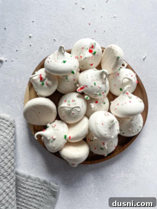 A close-up of beautifully piped peppermint meringues with crushed candy canes on top.