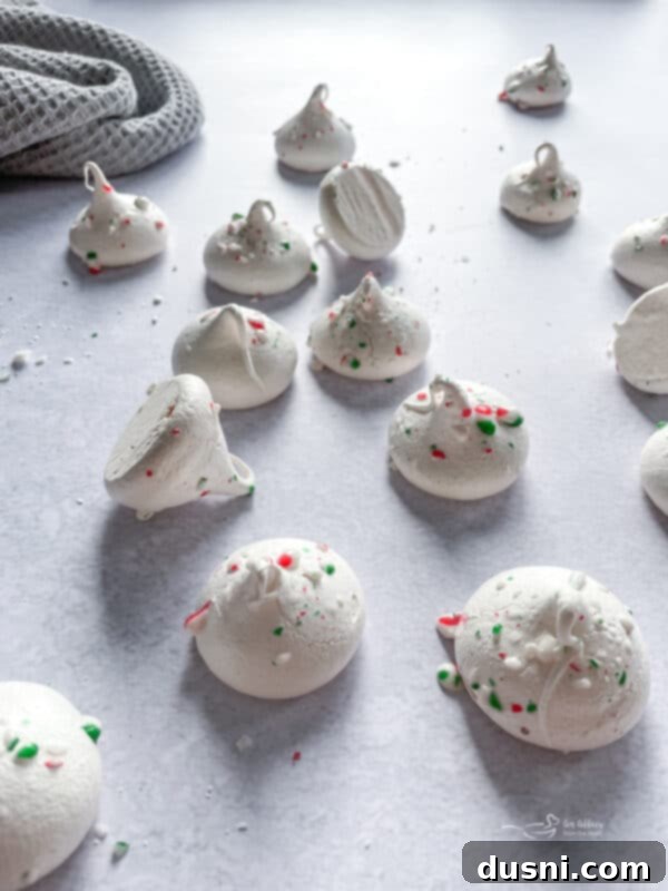 Close up of peppermint meringues sprinkled with crushed candy canes on a baking sheet.