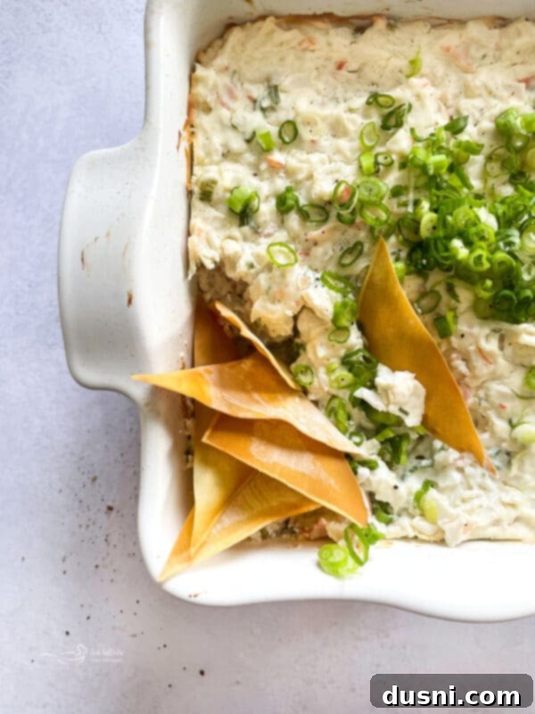 Savory Crab Rangoon Dip 2 Warm Crab Rangoon Dip served in a white baking dish with crispy wonton chips on the side.