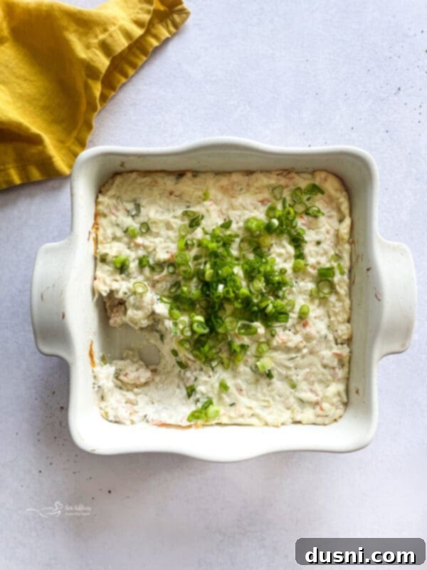 Savory Crab Rangoon Dip 12 A baking dish with creamy Crab Rangoon Dip, garnished with green onions and surrounded by golden wonton chips.