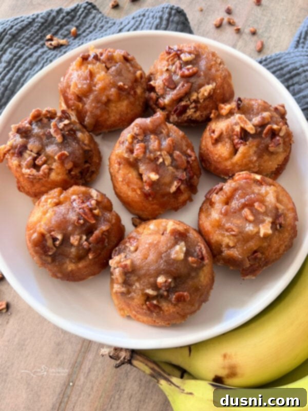 Banana Pecan Swirls 2 Close-up of golden brown banana pecan sticky rolls in a muffin tin, topped with glossy pecan caramel.