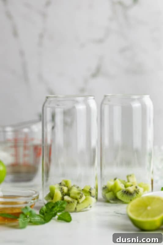 Vibrant Kiwi Mojito 4 Step one: Peeled and diced kiwifruit at the bottom of two tall cocktail glasses.