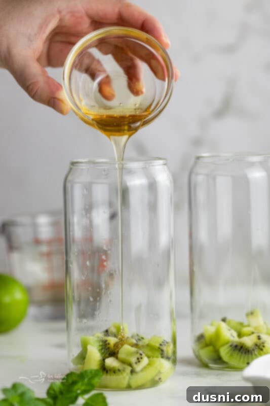 Vibrant Kiwi Mojito 6 Step three: A muddler pressing down on kiwi, mint, lime, and honey in a cocktail glass.