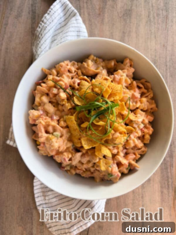 Loaded Frito Corn Salad 12 A bowl of Frito Corn Salad on a wooden table with a side of Frito chips.