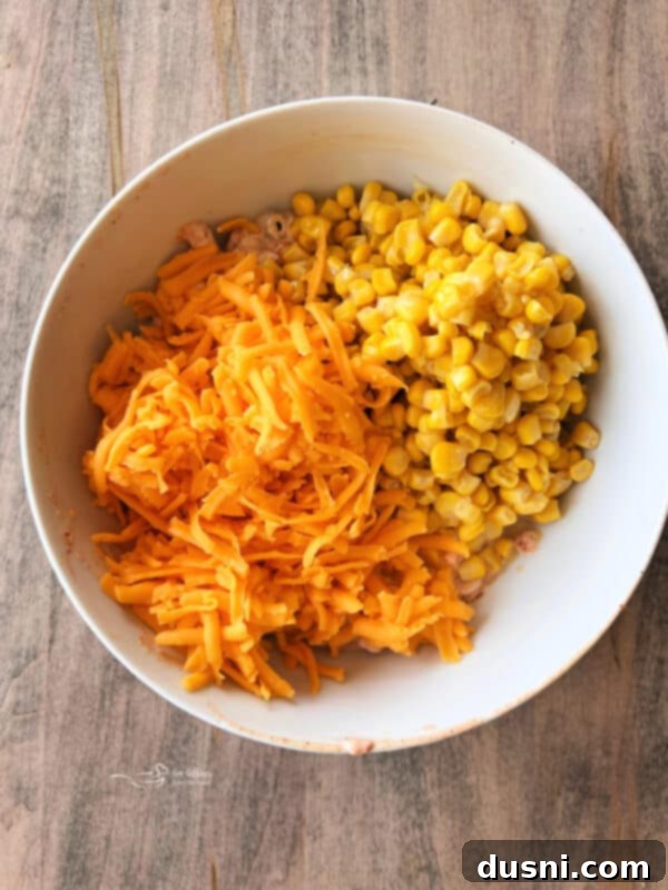 Loaded Frito Corn Salad 6 Step 2: Folding in corn kernels and shredded cheese into the creamy mixture.