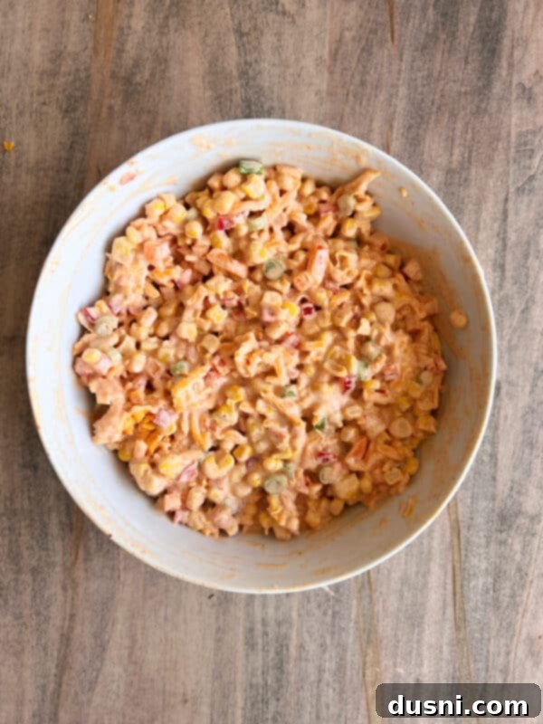 Loaded Frito Corn Salad 7 Step 3: A bowl of Frito Corn Salad mixture covered with plastic wrap, ready for chilling.