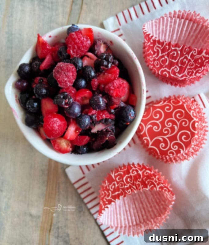Muffin liners being placed in a muffin tin with a bowl of berries
