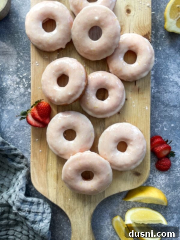 Sun-Kissed Strawberry Lemonade Donuts 3 Three strawberry lemonade donuts on a white plate with fresh fruit