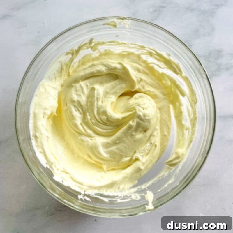 Dreamy Marshmallow Cloud Cheesecake 10 Heavy whipping cream being beaten in a stand mixer, forming stiff peaks for the marshmallow cheesecake.