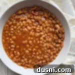Grandma's Heirloom Baked Beans 8 A white bowl filled with Grandma's Baked Beans, garnished with fresh parsley.