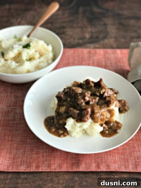 Tender Beef Tips in Rich Gravy 2 Tender Beef Tips & Gravy served over creamy mashed potatoes, garnished with fresh herbs.