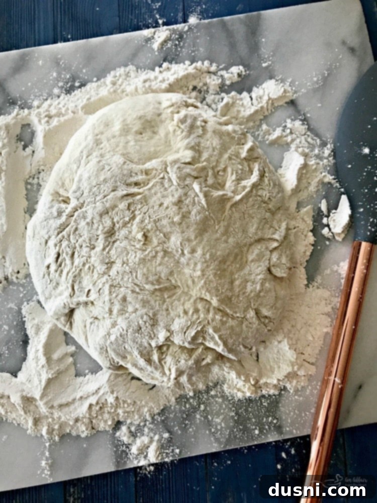 Sticky no-knead bread dough in a bowl, covered with plastic wrap, rising on a counter.