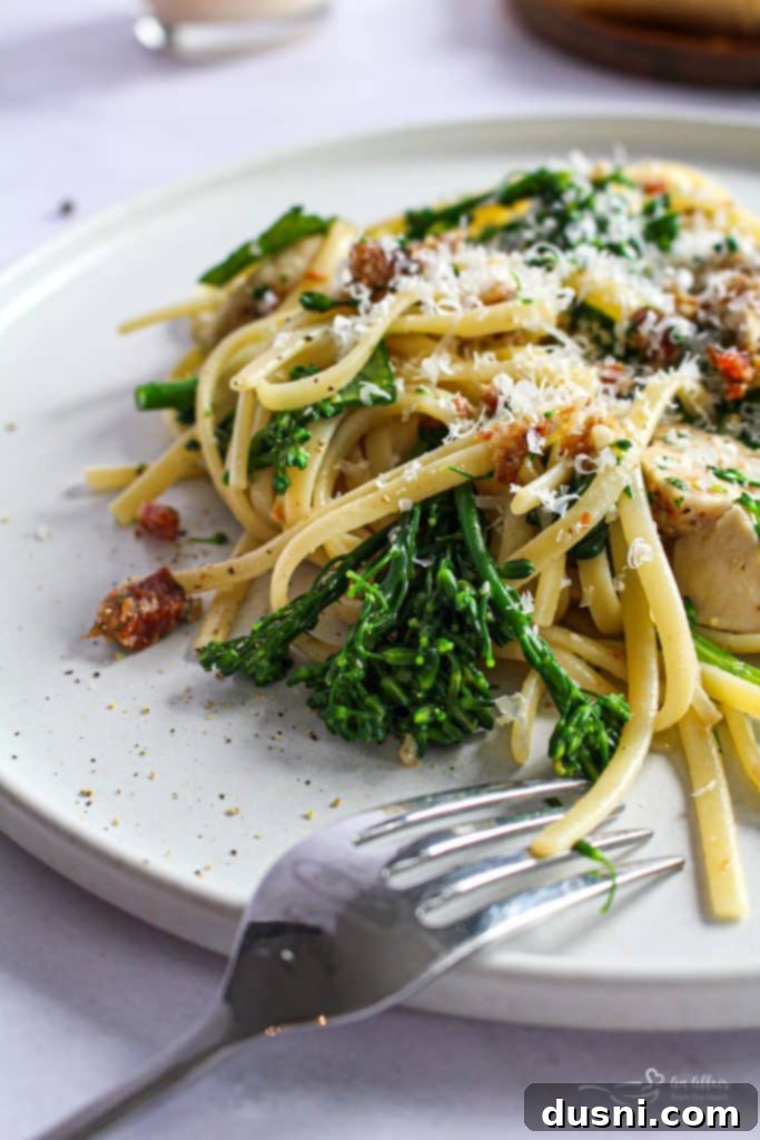 A vibrant bowl of creamy chicken carbonara with linguine, chicken, bacon, broccoli, and spinach, garnished with fresh parsley and Parmesan cheese.