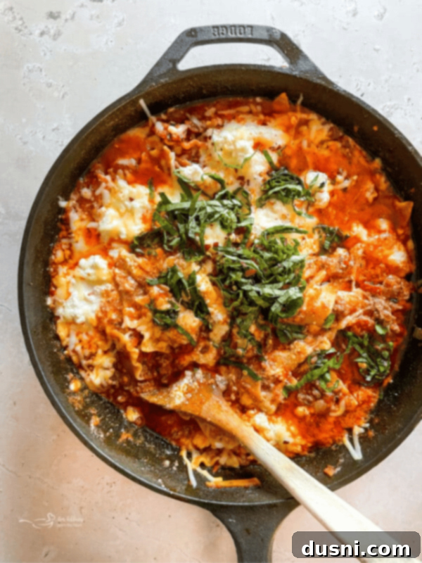 Hearty One-Pan Chili Mac 18 Overhead shot of skillet lasagna with a serving spoon in it, showcasing layers of cheese and sauce.