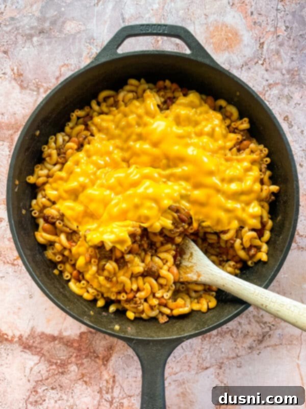 Hearty One-Pan Chili Mac 10 Cooked macaroni being folded into the chili mixture in a skillet.