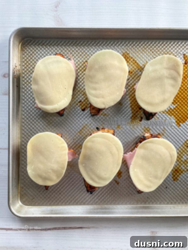 Smoky Mountain Chicken assembled with ham and provolone cheese on a baking sheet, ready for final baking