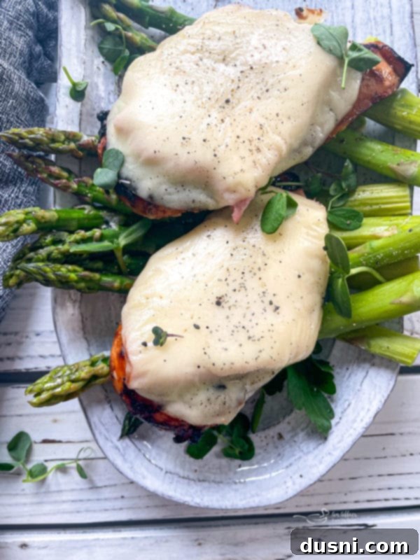 Grilled Smoky Mountain Chicken topped with melted provolone cheese and ham, served with a side of fresh asparagus