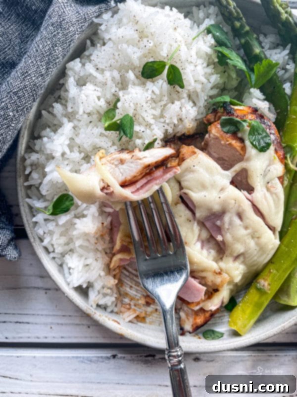 A fork piercing into a piece of Smoky Mountain Chicken, showing the layers of cheese and ham