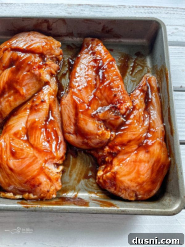 Chicken breasts being coated in barbecue sauce within a zip-top bag for marination