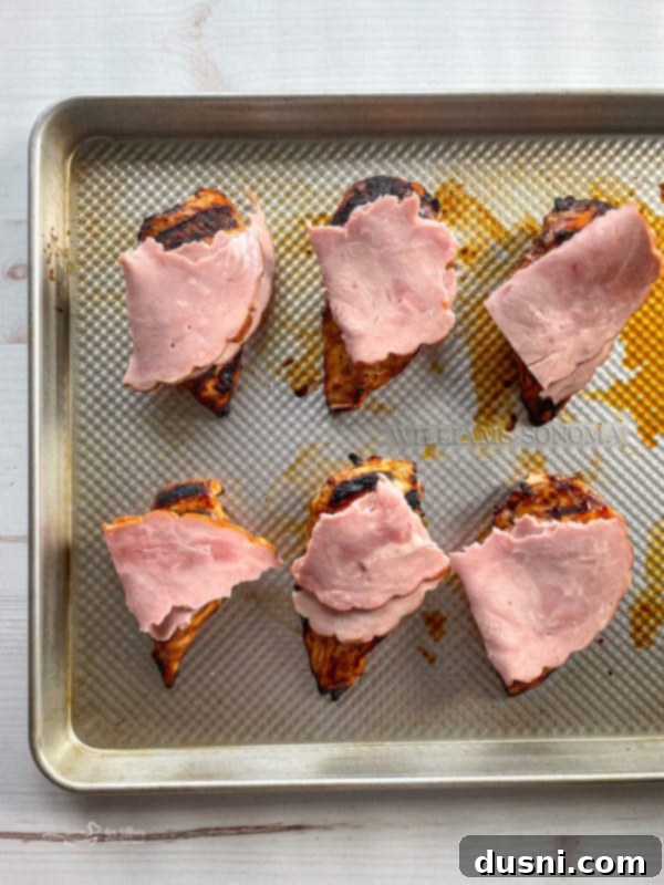 Cooked chicken breasts on a baking sheet, generously topped with sliced ham