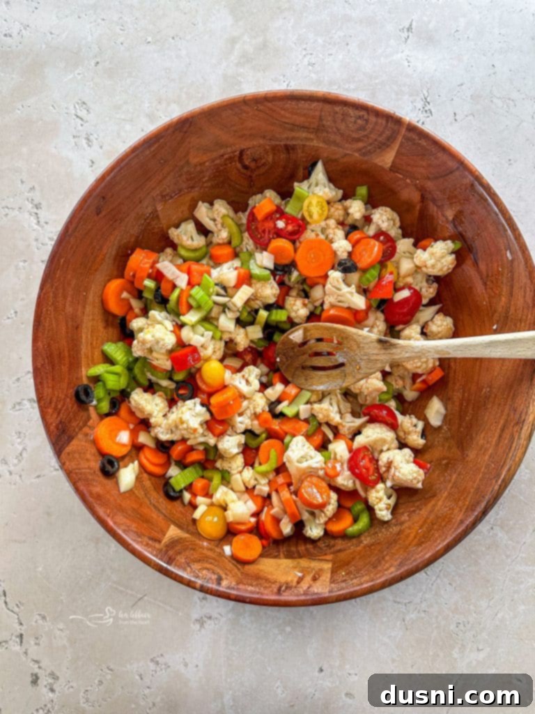 A person stirring dressing into a bowl of marinated vegetables.