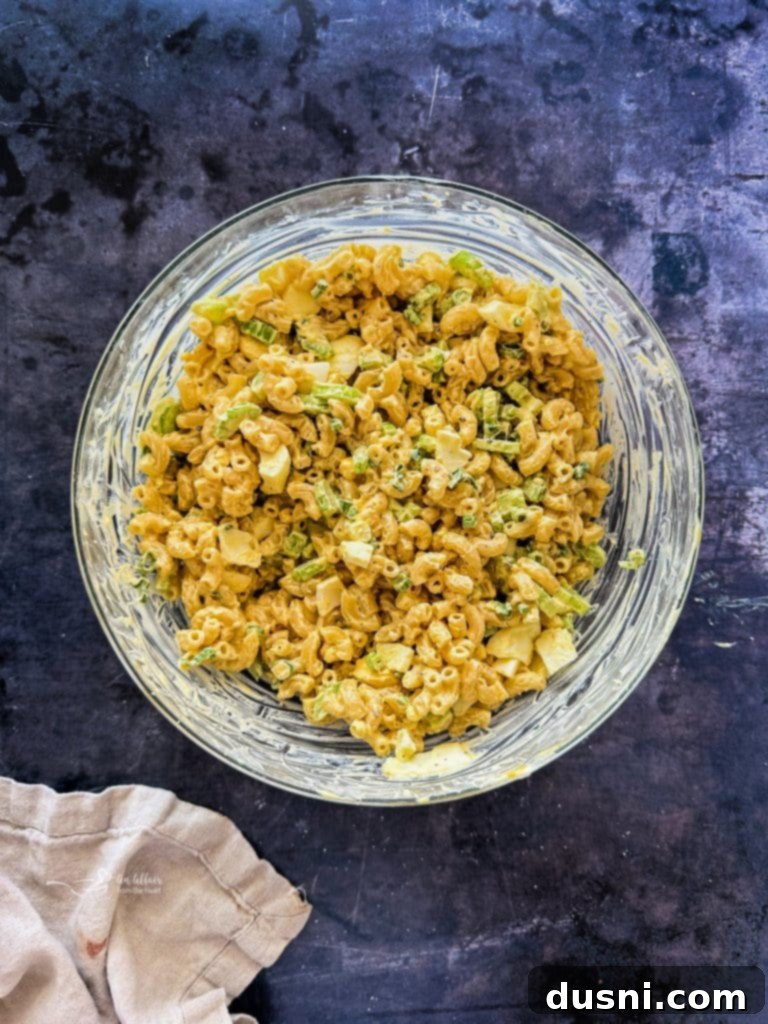 Mayonnaise and mustard being stirred into the macaroni and vegetable mixture.