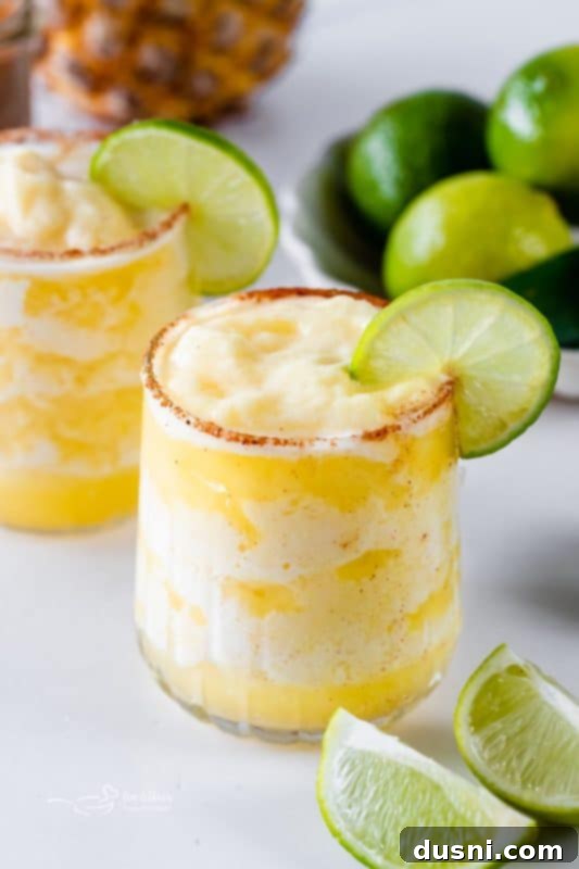 Close-up of Frozen Pineapple Margaritas garnished with pineapple and mint