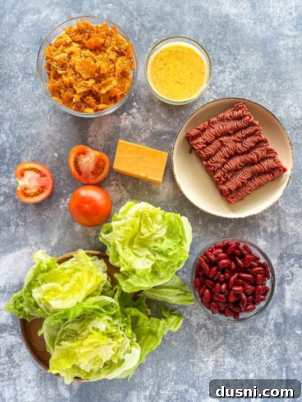 Ultimate Doritos Taco Salad 4 Ingredients for Doritos Taco Salad laid out on a table, including a bag of Doritos, lettuce, ground beef, cheese, and tomatoes.