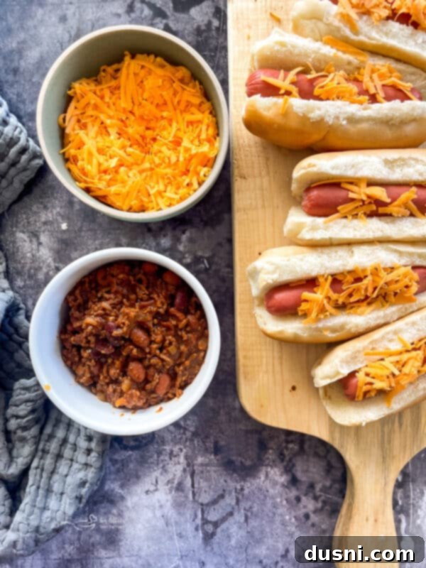 Chili cheese dogs lined up on a baking sheet, ready to be served