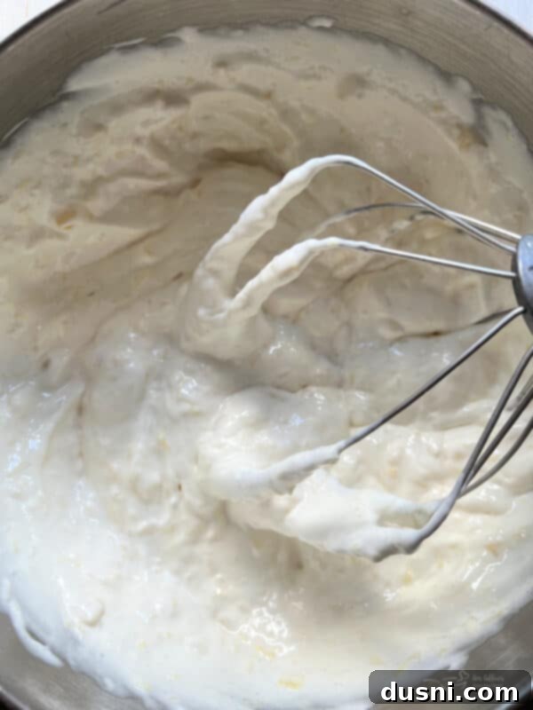 Angel food cake mix and crushed pineapple being combined in a large bowl with an electric mixer on low speed