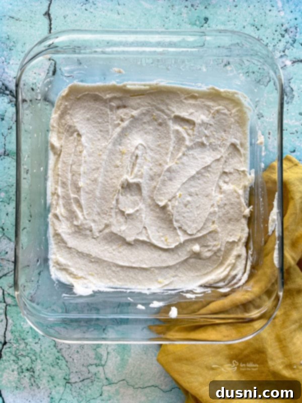 lemon brownie batter spread evenly into a parchment-lined 8x8 inch baking dish, ready for the oven