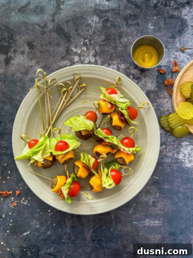 A hand placing a loaded skewer into a Bacon Cheeseburger Meatball