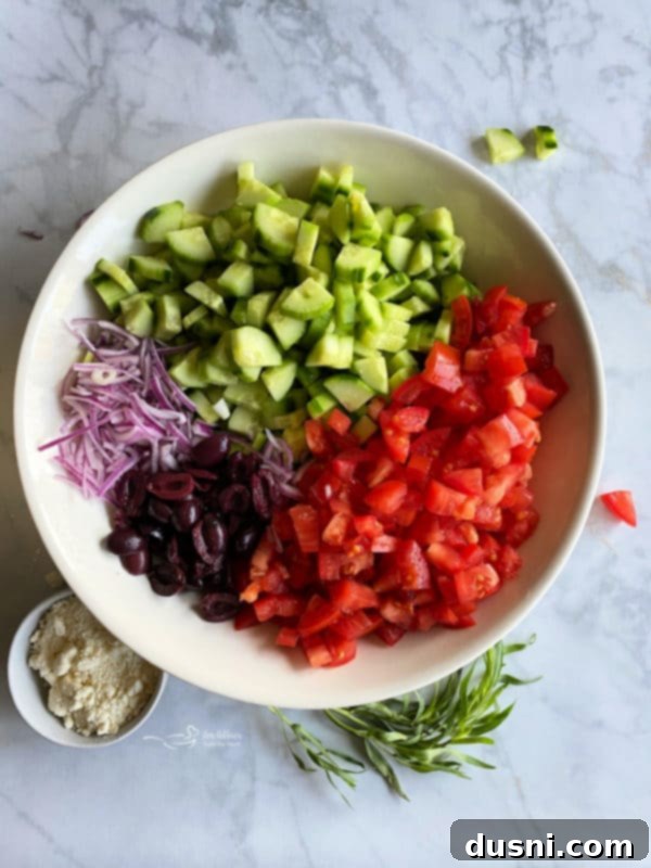 Hellenic Cucumber Medley 3 Close-up of fresh tomatoes, Kalamata olives, cucumbers, and thinly sliced red onion in a white bowl, ready for dressing.